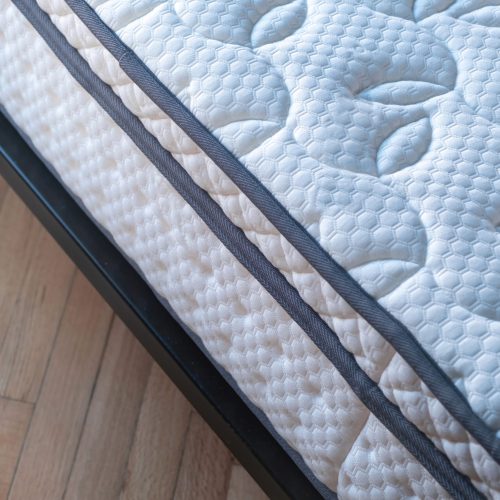 Mattress new and clean on a bed close up. Home bedroom interior detail, high angle view, wooden floor background. Comfort and healthy sleep and relaxation